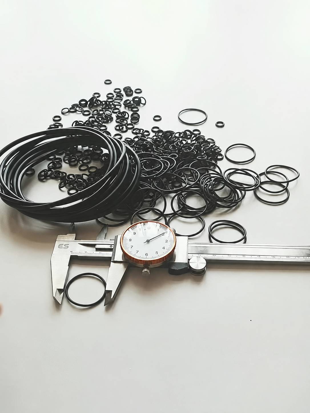 Assorted black rubber O rings beside a dial caliper