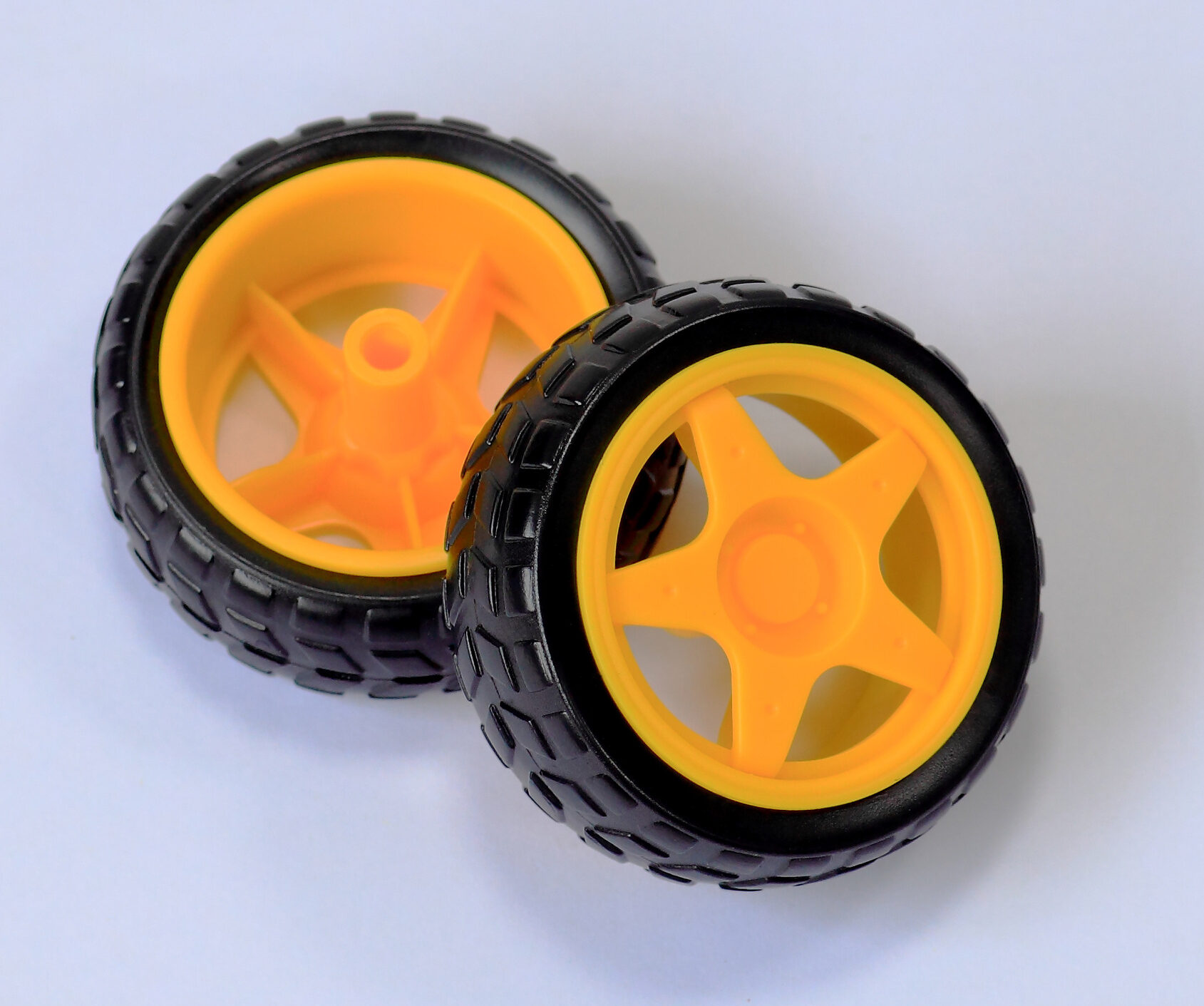 Two black rubber robot wheels with yellow spoked hubs, front view